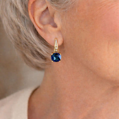 Aretes de argolla con piedra zafiro mística, hechos por Rose & Oliver, con detalle de piedras azules y acabado en metal brillante.